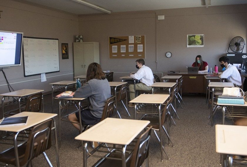 Students sitting separately in a classroom with masks on.