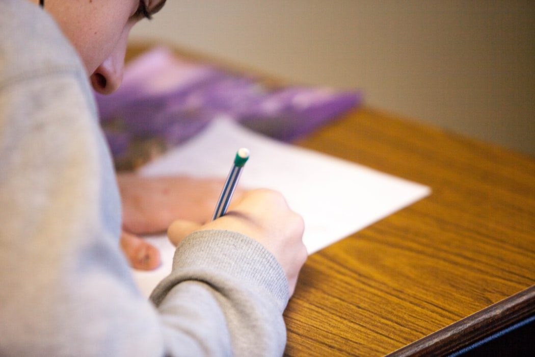 A child writing with a pencil on paper at a wooden desk.